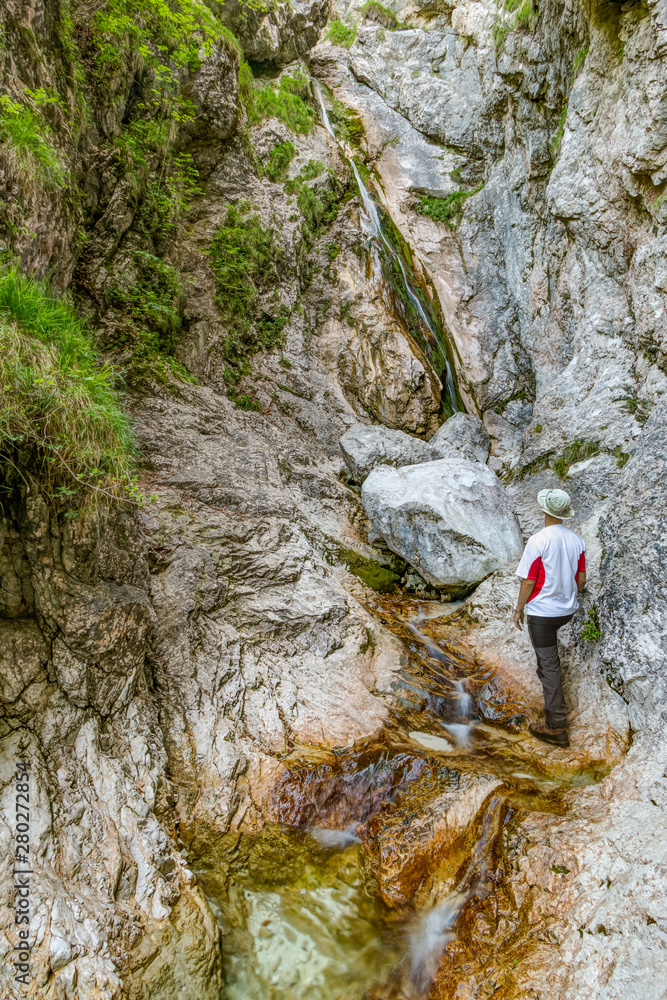 A mountaineer standing and enjoying the view of the Orglice waterfall in Kamniska Bistrica valley in Kamnik-Savinja Alps, Slovenia