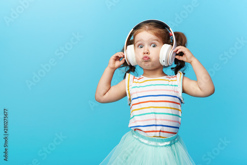 Obraz na płótnie Happy smiling child enjoys listens to music in headphones over colorful bleu background. Vivid and fun emotions, happy child with pleasure listens to songs in wireless headphones w salonie