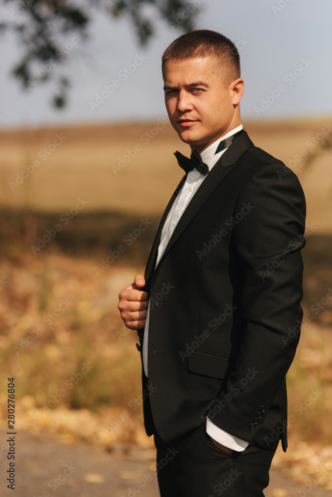Young man walking in the park. Handsome groom in black suit Young man walking in the park. Handsome groom in black suit