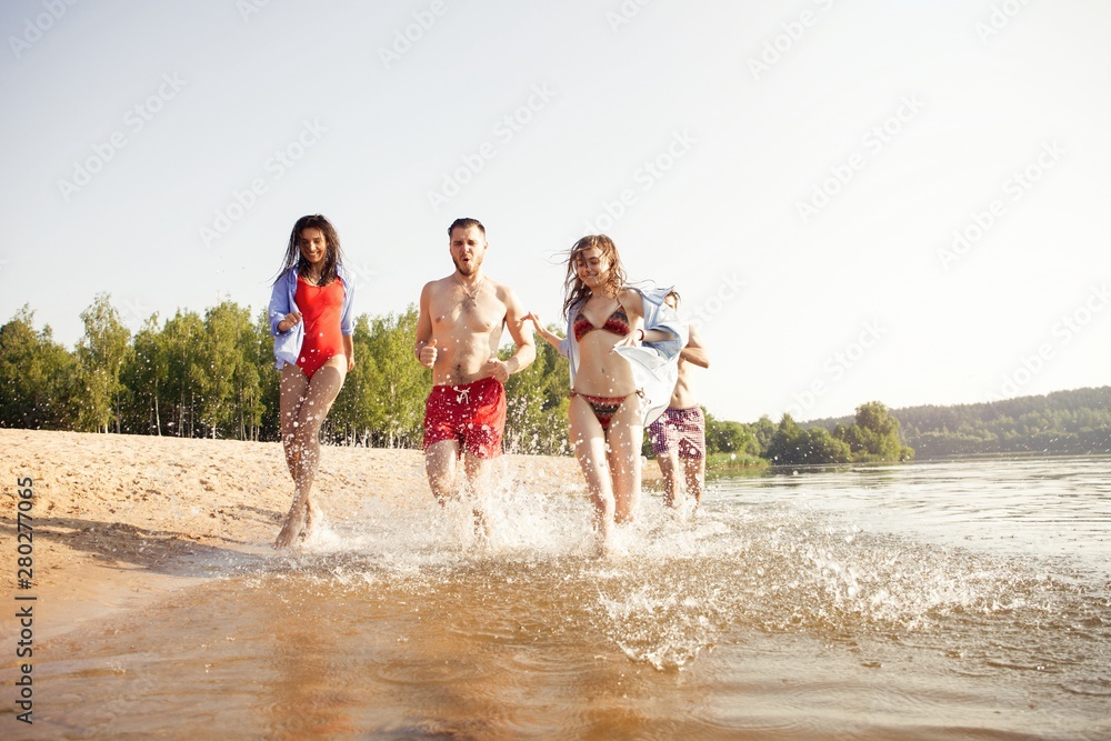 Group of happy friends running in to water - active people having fun on the beach on vacation