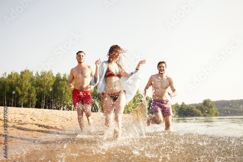 Group of happy friends running in to water - active people having fun on the beach on vacation