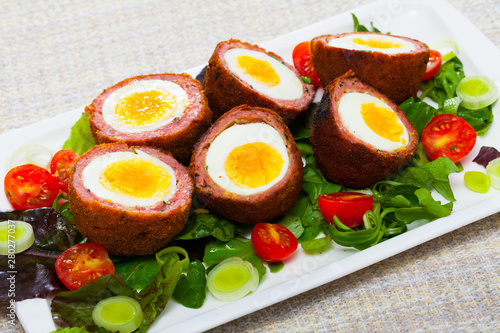 Dish of traditional Scottish cuisine of scotch eggs served with greens, leek and tomatoes at plate