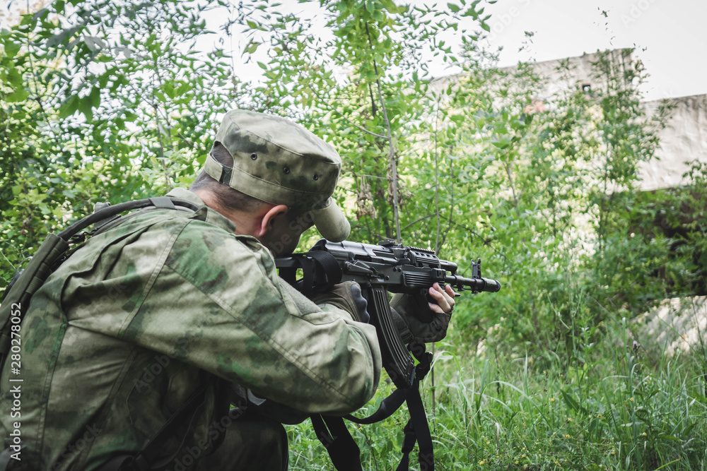 Fototapeta premium military crouching aims from a Kalashnikov in the woods