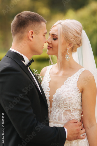 Groom kiss his bride in nose. Portrait of newlyweds outside
