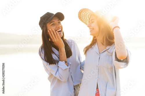 Two beautiful young women strolling on a beach. Female friends walking on the beach and laughing on a summer day.
