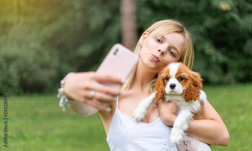 portrait of beautiful women in the park, hugging with the spaniel dog and making selfie by smartphone