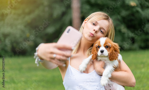 portrait of beautiful women in the park, hugging with the spaniel dog and making selfie by smartphone