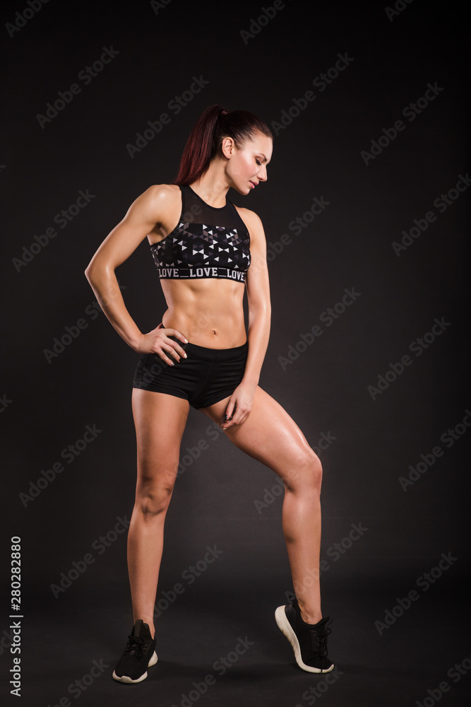 Attractive young woman in sportswear posing on black background