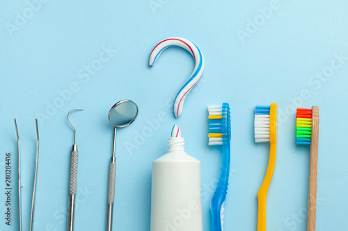 Question mark from toothpaste. Tube of colored toothpaste and toothbrush and dentist tools, mirror, hook on blue background. The concept of choosing good toothpaste for brushing your teeth