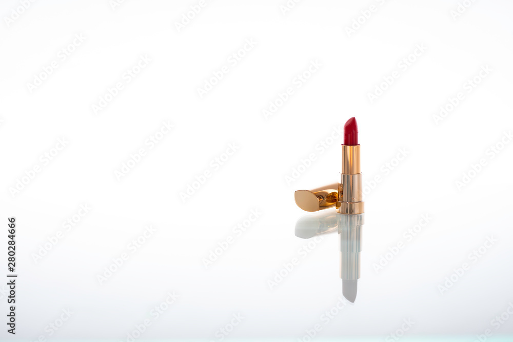 Dark red lipstick with golden housing with reflection on glass isolated on white background