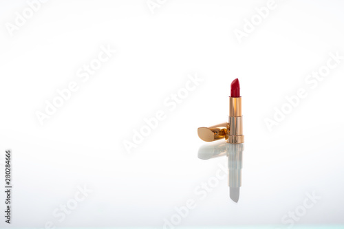 Dark red lipstick with golden housing with reflection on glass isolated on white background photo