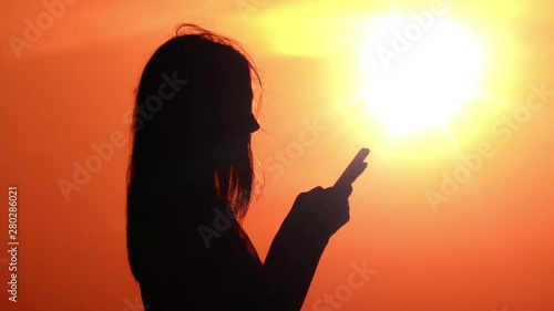 silhouette profile girl holding smartphone typing message on the background sky with golden rising sun photo