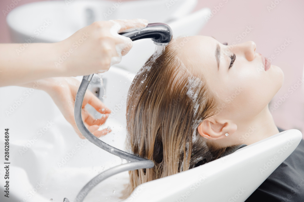 Fototapeta premium Washing hair of beautiful blonde girl in beauty salon, coloring