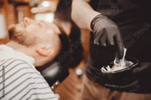 Brush for shaving beard along with bowl, blurred background of hair salon for men, barber shop