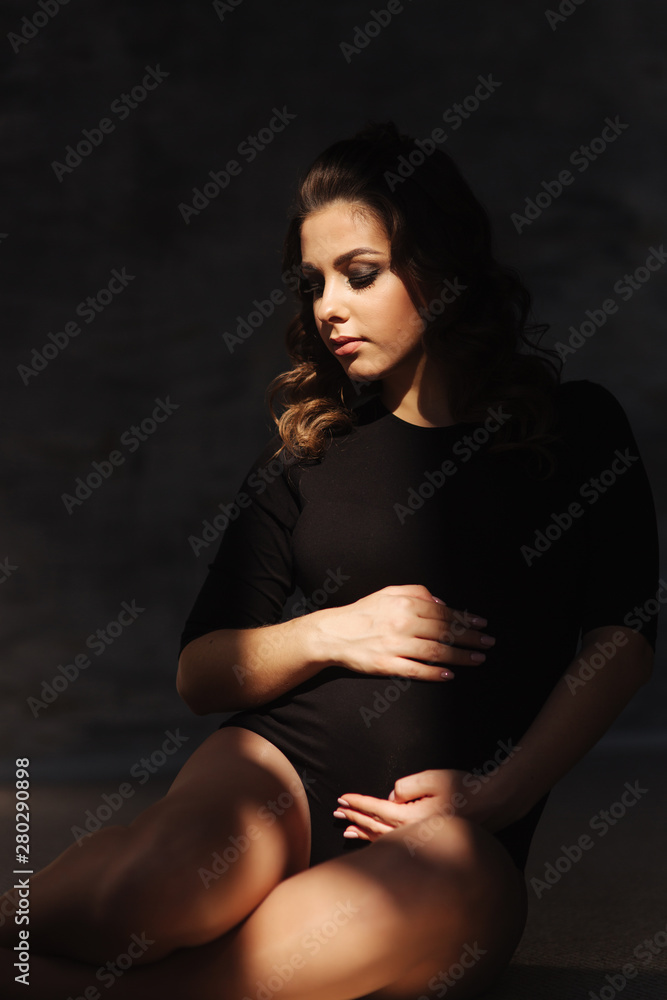 Young pregnant woman sit near the window. Sun rays fall on woman