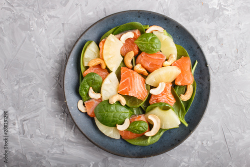 Fresh salmon with pineapple, spinach and cashew in blue ceramic plate on a gray concrete background.