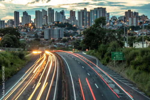 Trail of light caused by vehicular traffic in SP-294  Comandante Joao Ribeiro Barros Highway with buildings from downtown in the background  in Mar  lia  during a late afternoon.