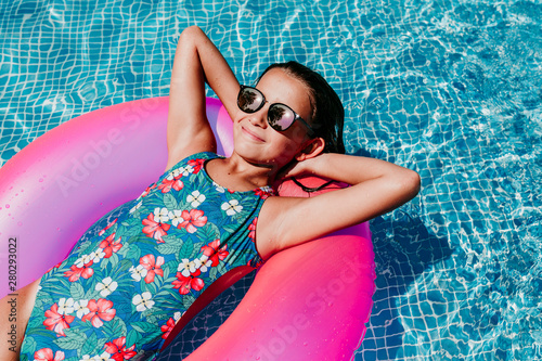 Canvastavla beautiful teenager girl floating on pink donuts in a pool