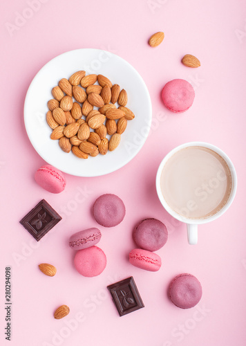Purple and pink macaron or macaroon cakes with cup of coffee and almonds on pastel pink background.