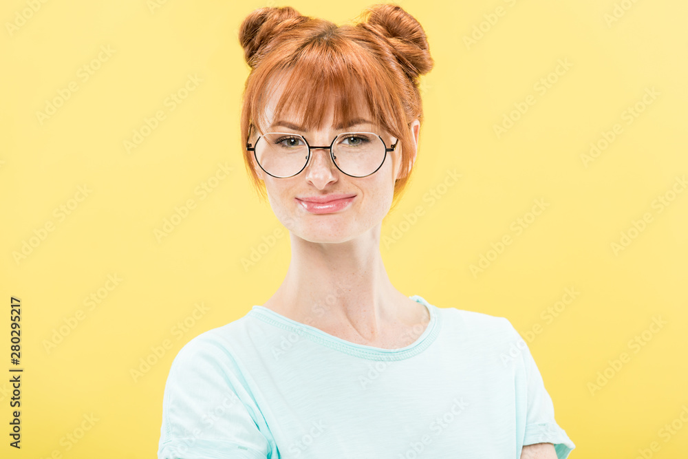 front view of smiling redhead girl in glasses and t-shirt looking at camera isolated on yellow