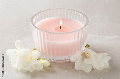 Lit candle and beautiful flowers on grey marble table