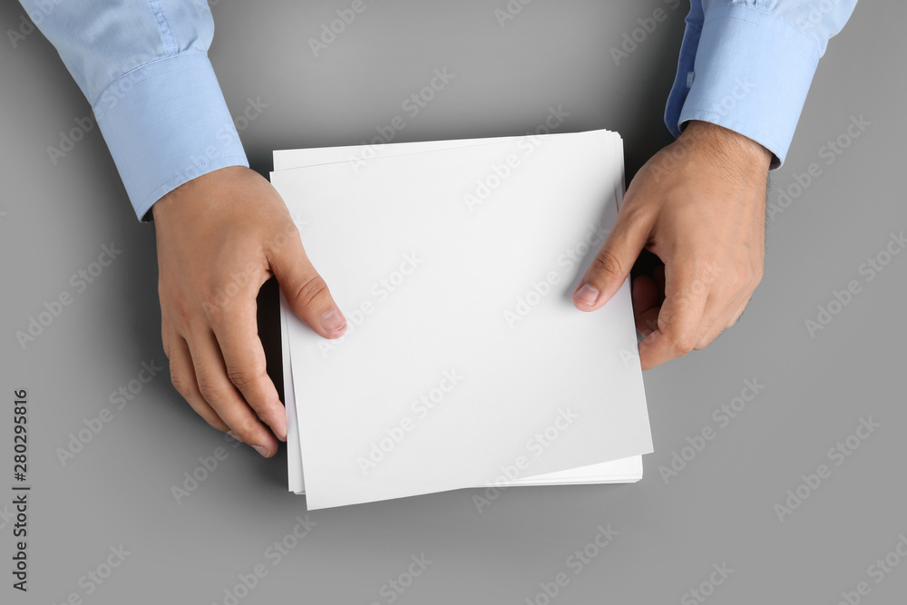 Man holding blank paper sheets for brochure at grey table, top view. Mock up Man holding blank paper sheets for brochure at grey table, top view. Mock up