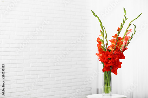Vase with beautiful gladiolus flowers on wooden table indoors. Space for text