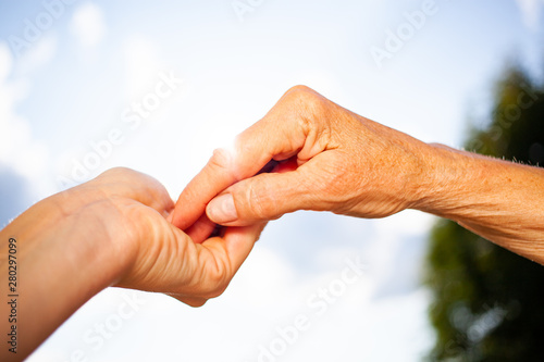 close-up of tender gesture between two generations. Young woman holding hands with a senior lady. Blue sky background © Melinda Nagy