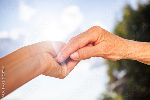 close-up of tender gesture between two generations. Young woman holding hands with a senior lady. Blue sky background © Melinda Nagy