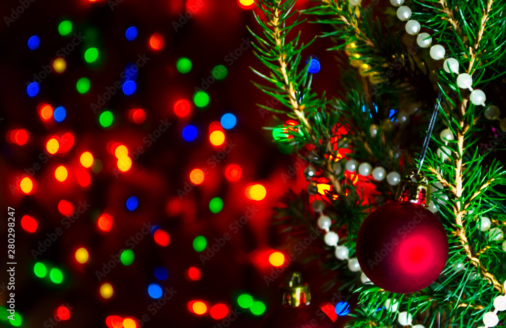 Red Christmas ball on Christmas tree with blurred lights. Christmas ball and lights on dark blur background. Christmas card with blurred lights. Background with bokeh of Christmas lights. Copy space.
