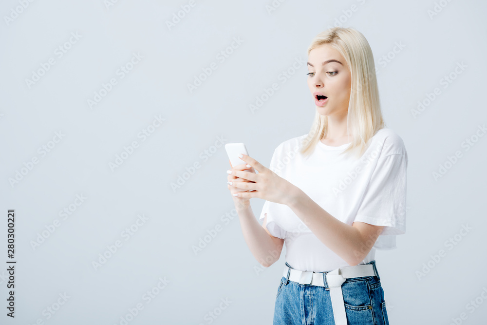 beautiful surprised blonde girl using smartphone isolated on grey beautiful surprised blonde girl using smartphone isolated on grey