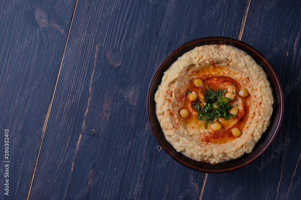 Classic hummus with hot pepper in a clay plate on a wooden table. National, vegetarian dish. General form. Classic hummus with hot pepper in a clay plate on a wooden table. National, vegetarian dish. General form.