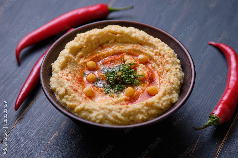 Classic hummus with hot pepper in a clay plate on a wooden table. National, vegetarian dish. General form. Classic hummus with hot pepper in a clay plate on a wooden table. National, vegetarian dish. General form.