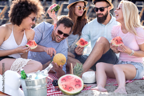 Happy young friends eating watermelon on the beach