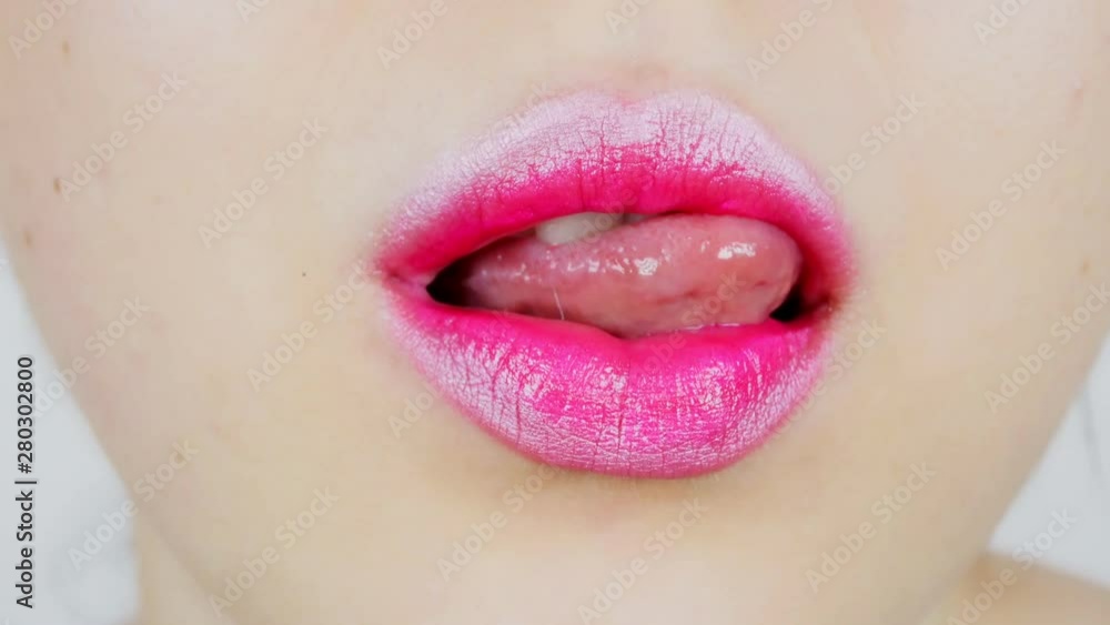 Extreme close-up of the lips of a young woman. A woman sexually licks bright full lips. She has a tongue piercing. Extreme close-up of the lips of a young woman. A woman sexually licks bright full lips. She has a tongue piercing.