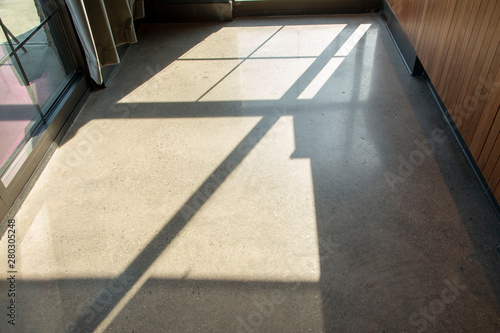 Window pane shadows cast down on the generic gray brown floor of a school, store, restaurant or office building.