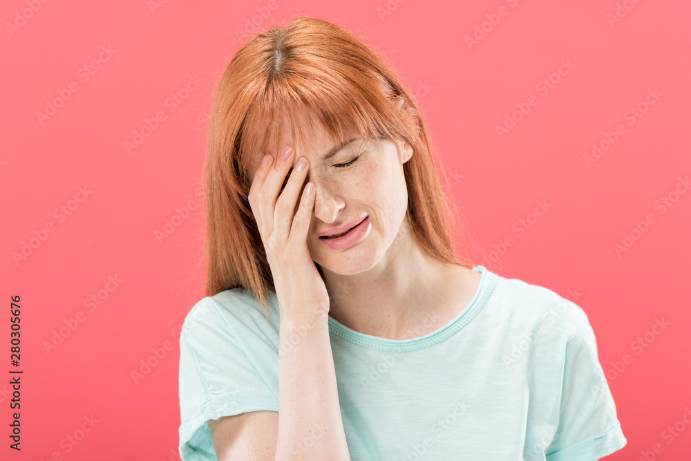 front view of young redhead woman in t-shirt with headache touching head isolated on pink