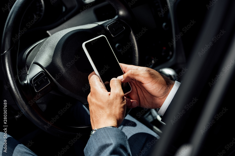 partial view of african american businessman in suit using smartphone in car at sunny day partial view of african american businessman in suit using smartphone in car at sunny day