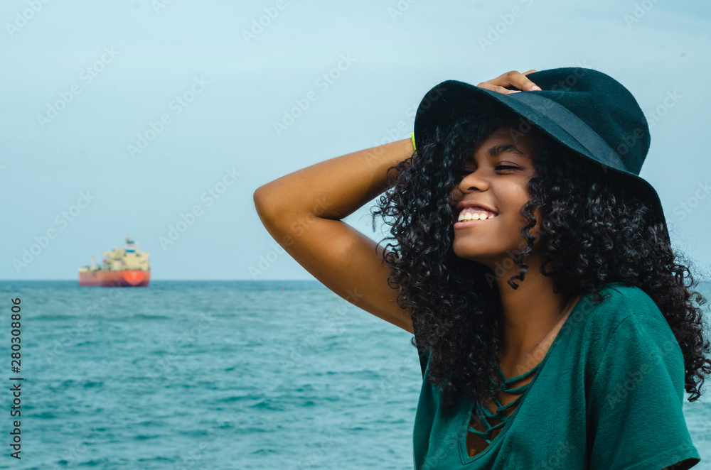 Young girl with black hair, laughing hair sitting on her back to the Caribbean Sea, enjoying a summer day with the wind in her hair, lifestyle portrait Young girl with black hair, laughing hair sitting on her back to the Caribbean Sea, enjoying a summer day with the wind in her hair, lifestyle portrait