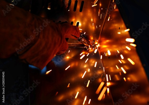 A Indian woman wearing a pink long sleeve jacket, safety welding mask and leather gloves, welding a metal case for computer server rack, with sparks