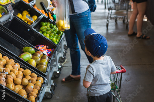 Curious toddler pusing small cart shopping with mother at farmers market. photo