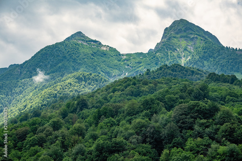 Green slopes and rocky peaks of high mountains in cloudy summer day © Dmitrii Potashkin
