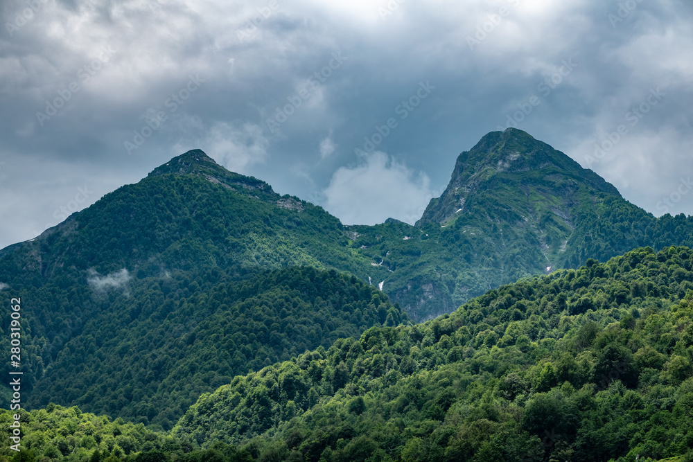 Green slopes and rocky peaks of high mountains in cloudy summer day