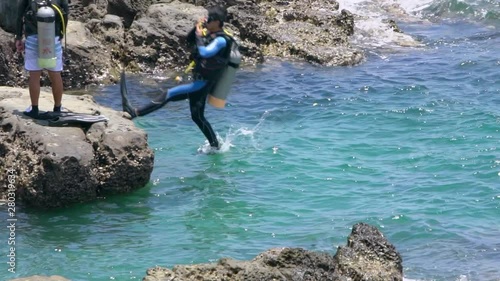 Slow Motion of scuba diver jumping in the water from rock of coast. People swimming in blue ocean with scuba diver's equipment at summer vacation of tropical island-Dan photo