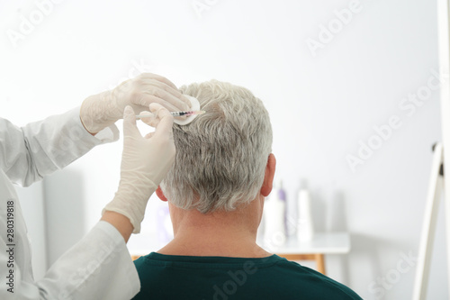 Senior man with hair loss problem receiving injection in salon