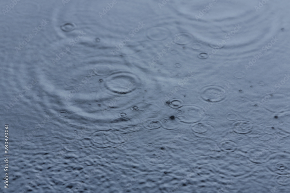 Rain drops falling down into puddle outdoors Rain drops falling down into puddle outdoors