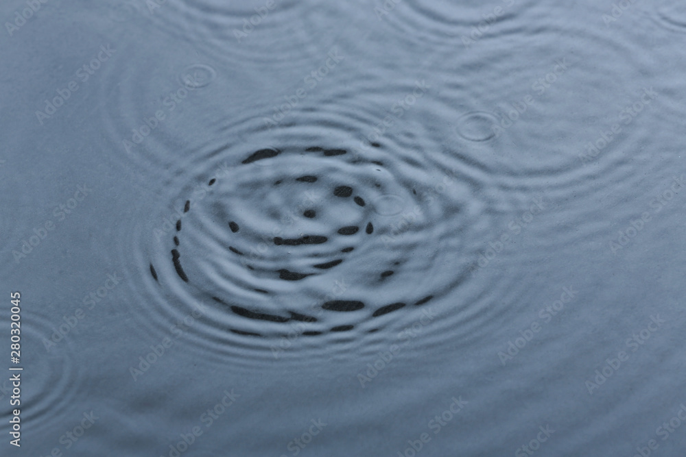 Rain drops falling down into puddle outdoors Rain drops falling down into puddle outdoors