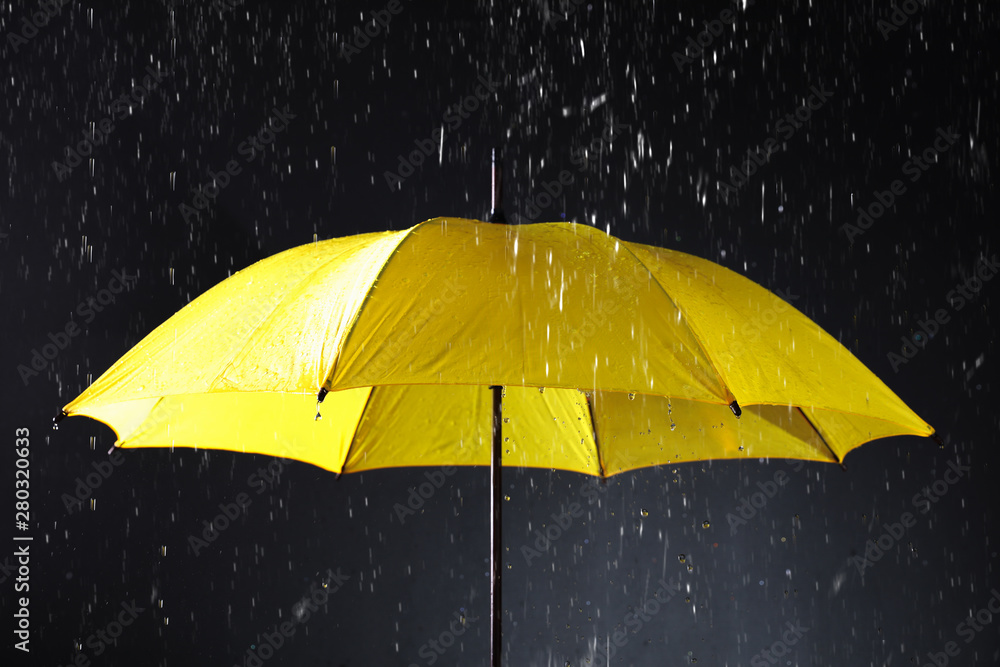 Bright umbrella under rain on dark background