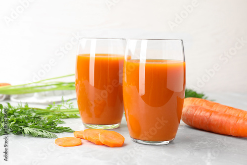 Glasses of drink and carrots on light table, space for text