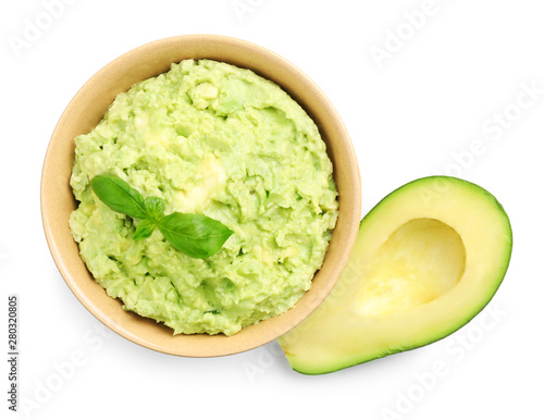 Bowl of tasty guacamole with basil and cut avocado on white background, top view photo
